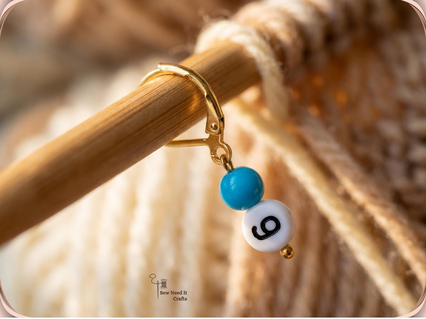 Close-up of a single gold-tone leverback stitch marker closed around a bamboo knitting needle, with a blue bead and a number 9 bead hanging below