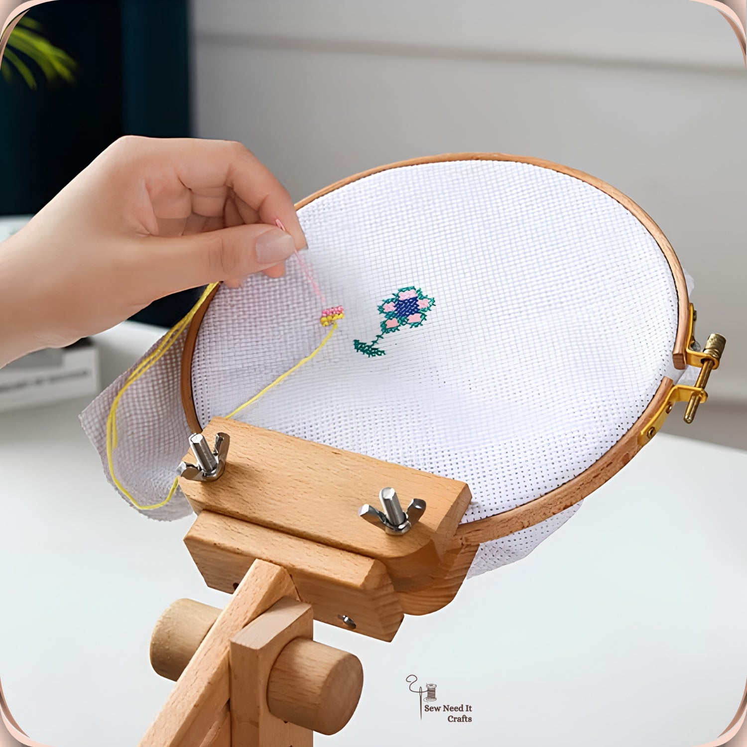 Close-up of a hand stitching a cross stitch flower in a hoop held by the beechwood embroidery stand