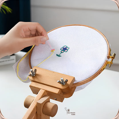 Close-up of a hand stitching a cross stitch flower in a hoop held by the beechwood embroidery stand
