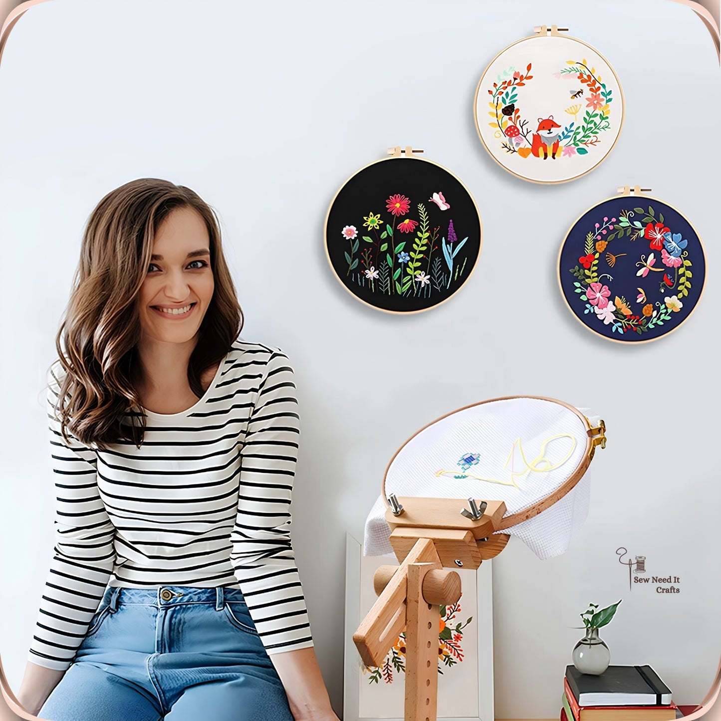Woman stitching at the beechwood clamp-on embroidery stand with four finished hoop artworks displayed on the wall behind her