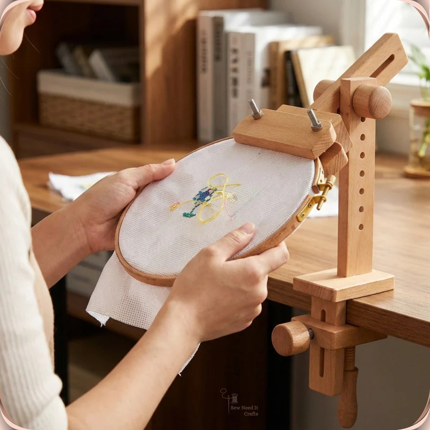 Hands adjusting an embroidery hoop mounted on the beechwood clamp-on stand at a wooden desk
