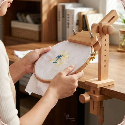 Hands adjusting an embroidery hoop mounted on the beechwood clamp-on stand at a wooden desk