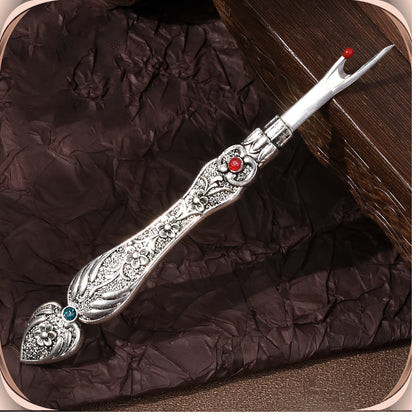 Antique Silver flat handle seam ripper on a dark plum background, showing the raised blossom engraving, the red crystal at the collar and the teal-green crystal in the tail