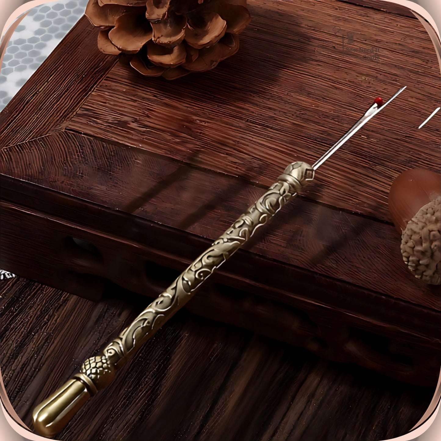 Antique Bronze round handle seam ripper resting on a dark wooden box, showing the scroll engraved slim handle, faceted bead and smooth fluted end