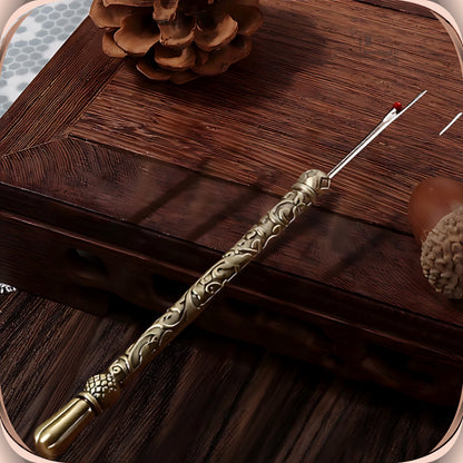 Antique Bronze round handle seam ripper resting on a dark wooden box, showing the scroll engraved slim handle, faceted bead and smooth fluted end