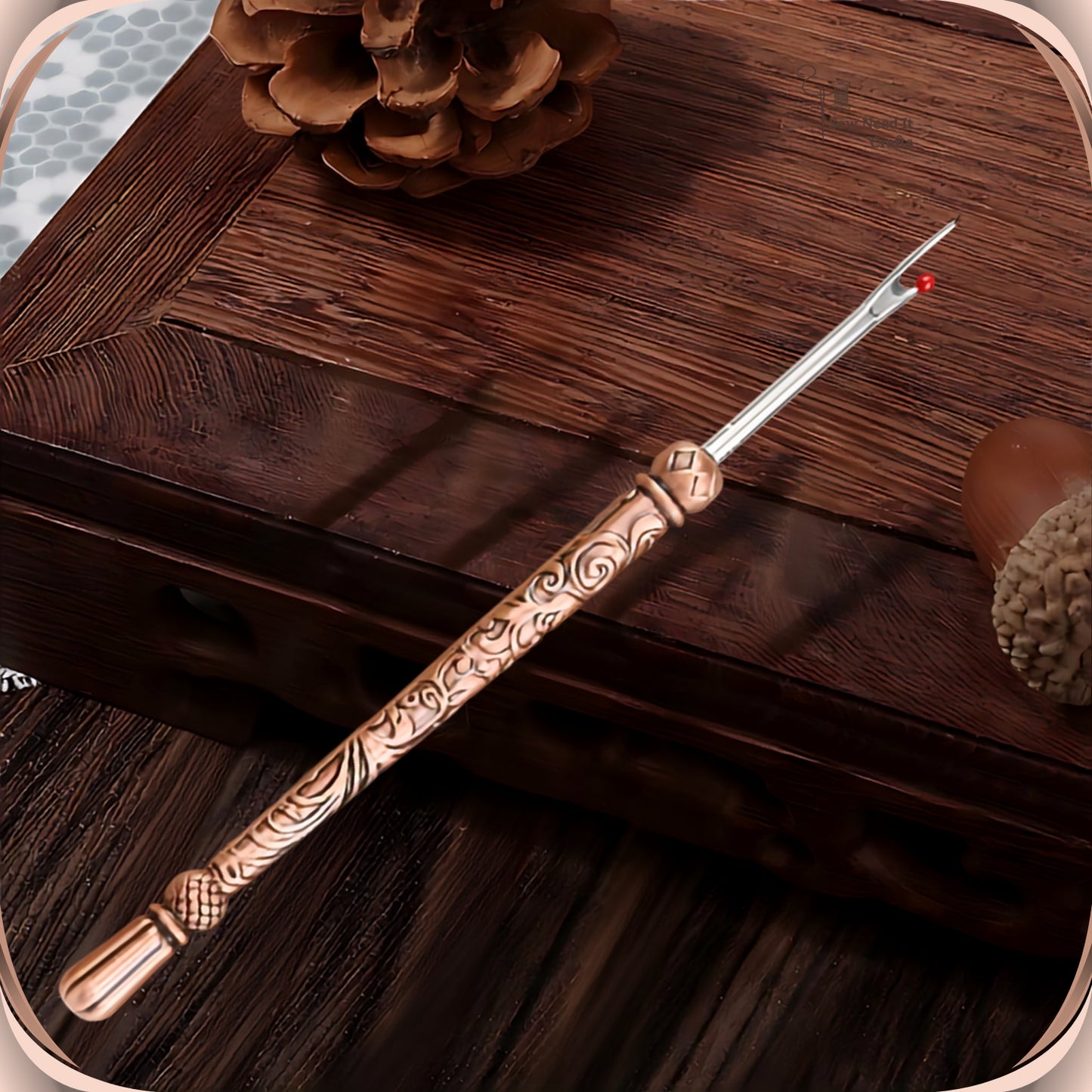 Antique Copper round handle seam ripper resting on a dark wooden box, showing the scroll engraved slim handle, faceted bead and smooth fluted end