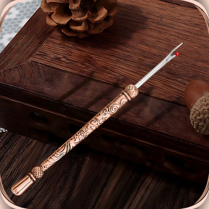 Antique Copper round handle seam ripper resting on a dark wooden box, showing the scroll engraved slim handle, faceted bead and smooth fluted end