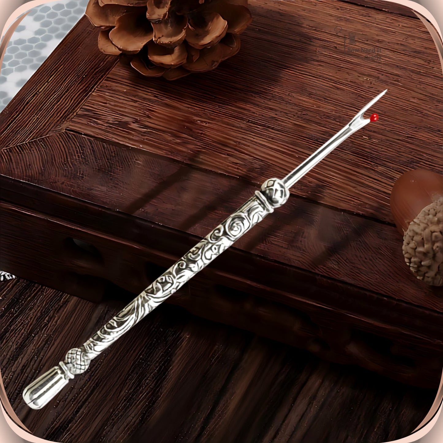 Antique Silver round handle seam ripper resting on a dark wooden box, showing the scroll engraved slim handle, faceted bead and smooth fluted end
