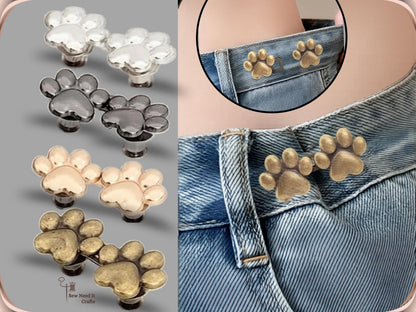 Paw waist adjuster buttons in silver, gunmetal, golden and bronze beside a golden pair fastened on a denim waistband