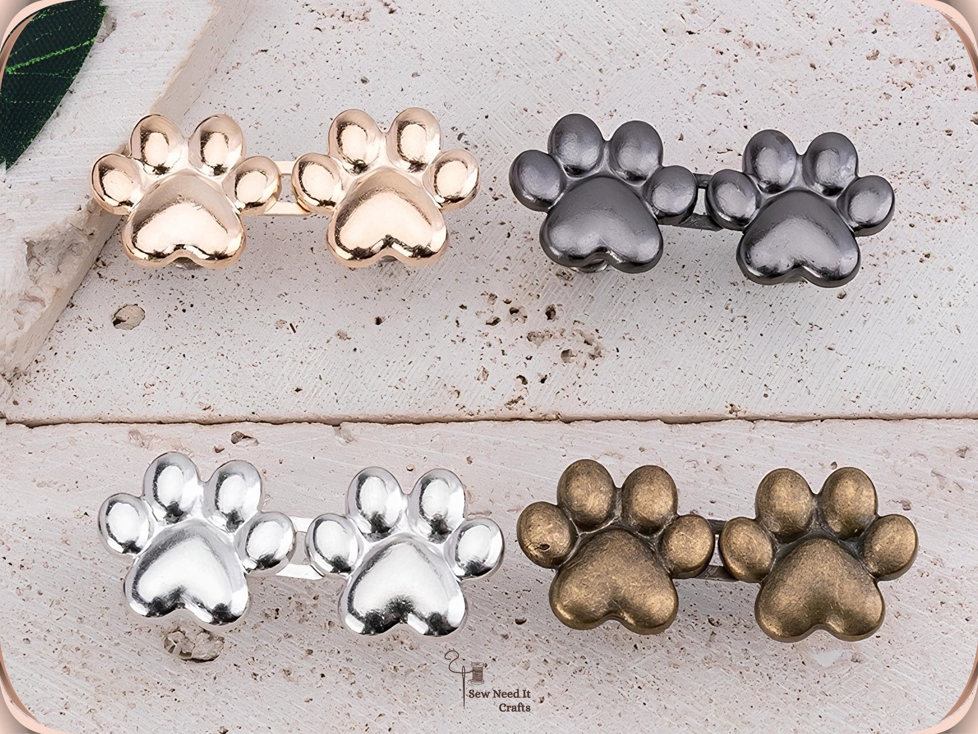Four pairs of paw print waist adjuster buttons in golden, gunmetal, silver and bronze on a white wood surface