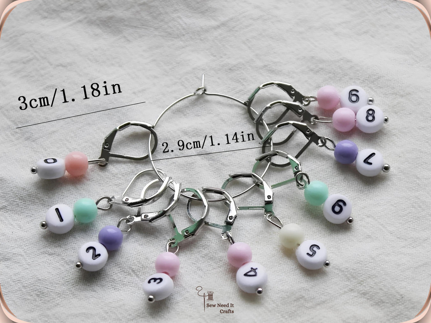 The full silver set of ten numbered stitch markers 0 to 9 on their storage hoop, one leverback clasp shown fully open, with each marker measuring 3cm or 1.18 inches and the hoop 2.9cm or 1.14 inches across