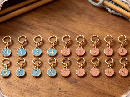 Blue and pink numbered stitch markers arranged in rows on a wooden surface with bamboo knitting needles and grey yarn