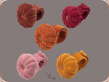 Five pumpkin wrist pin cushions on a grey background with their corduroy bands coiled behind them, in coffee, dark red, orange, dusty pink and dark yellow