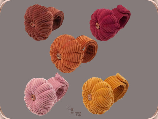 Five pumpkin wrist pin cushions on a grey background with their corduroy bands coiled behind them, in coffee, dark red, orange, dusty pink and dark yellow