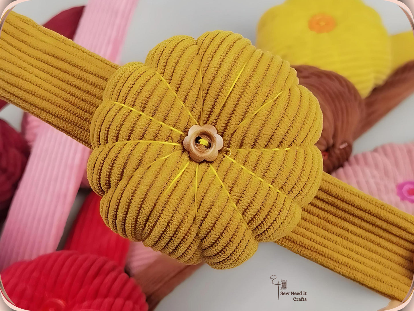 Close-up of a dark yellow corduroy pumpkin pin cushion with a wooden flower button at its centre, mounted across a matching corduroy band