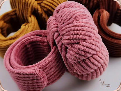Close-up of two dusty pink pumpkin pin cushions with their corduroy bands coiled into rings, showing how the snap-on band curls around the wrist