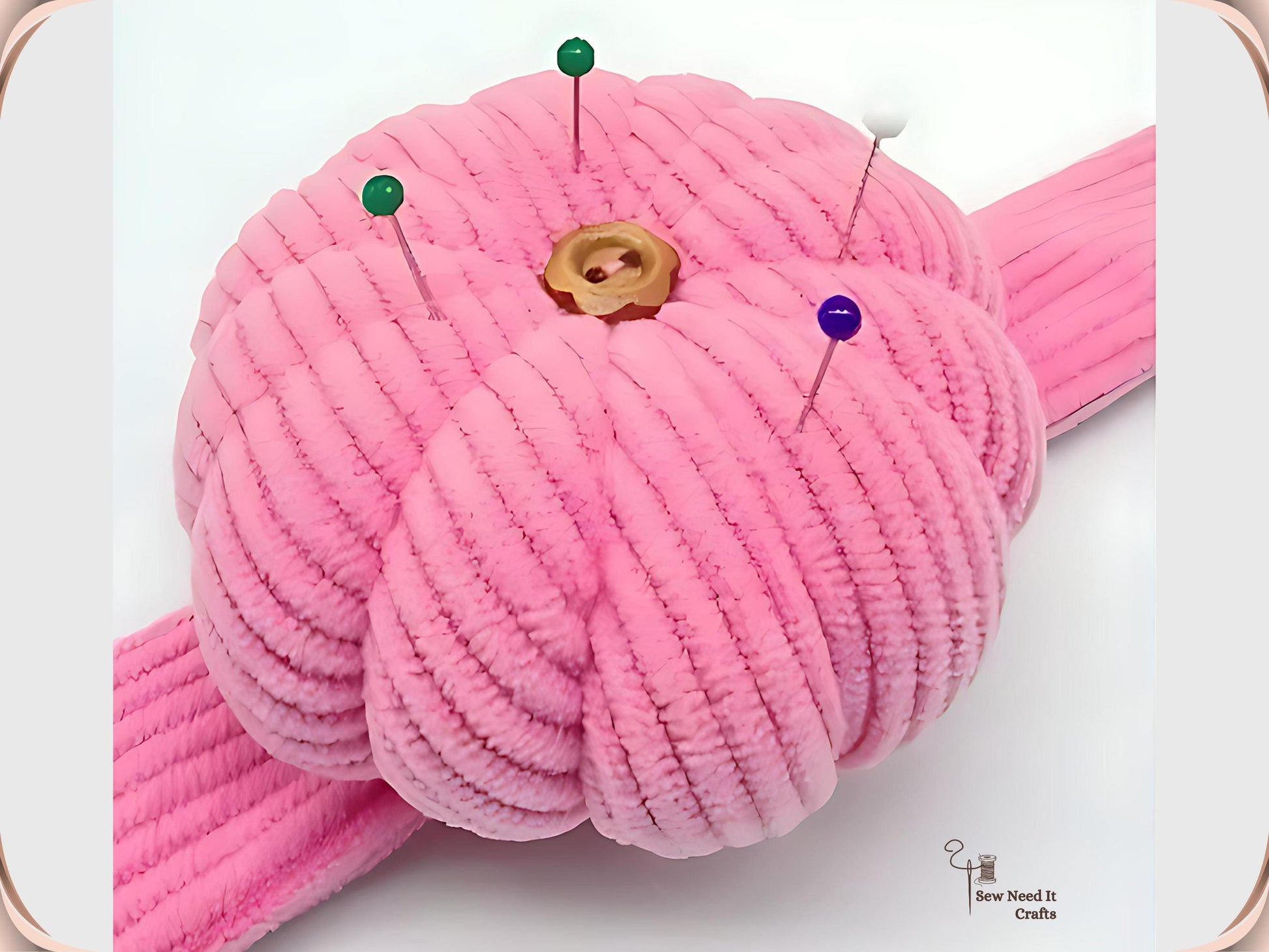 Close-up of a pink corduroy pumpkin pin cushion holding four glass-head pins in green, white and purple, with a wooden flower button at the centre