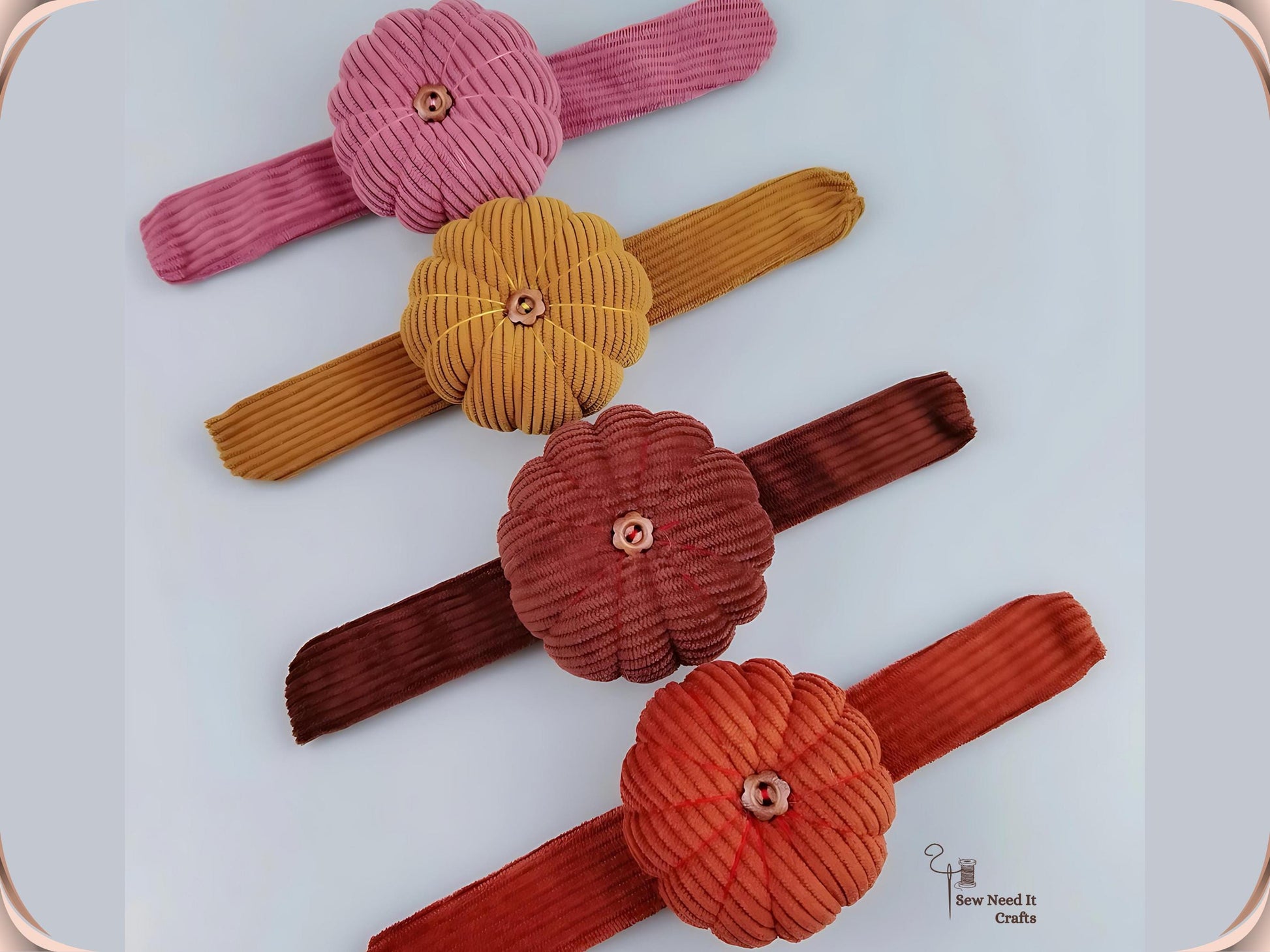 Four pumpkin wrist pin cushions laid flat in a row in dusty pink, dark yellow, coffee and red, showing the full length of each corduroy band
