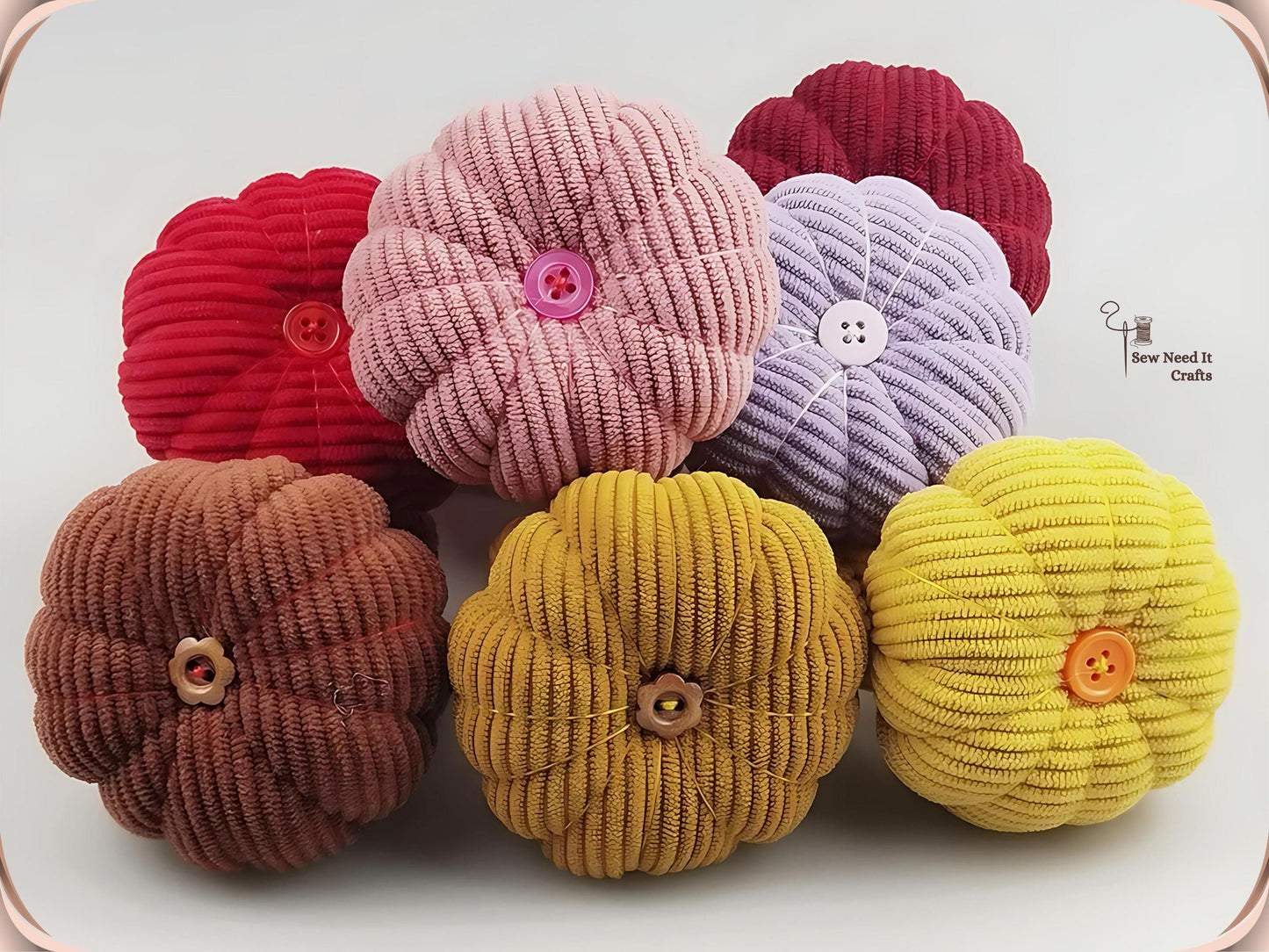 Six corduroy pumpkin pin cushions grouped together in red, dusty pink, dark red, purple, coffee, dark yellow and yellow, showing the ribbed texture and button centres