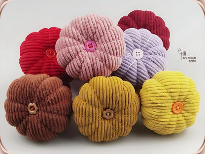 Six corduroy pumpkin pin cushions grouped together in red, dusty pink, dark red, purple, coffee, dark yellow and yellow, showing the ribbed texture and button centres