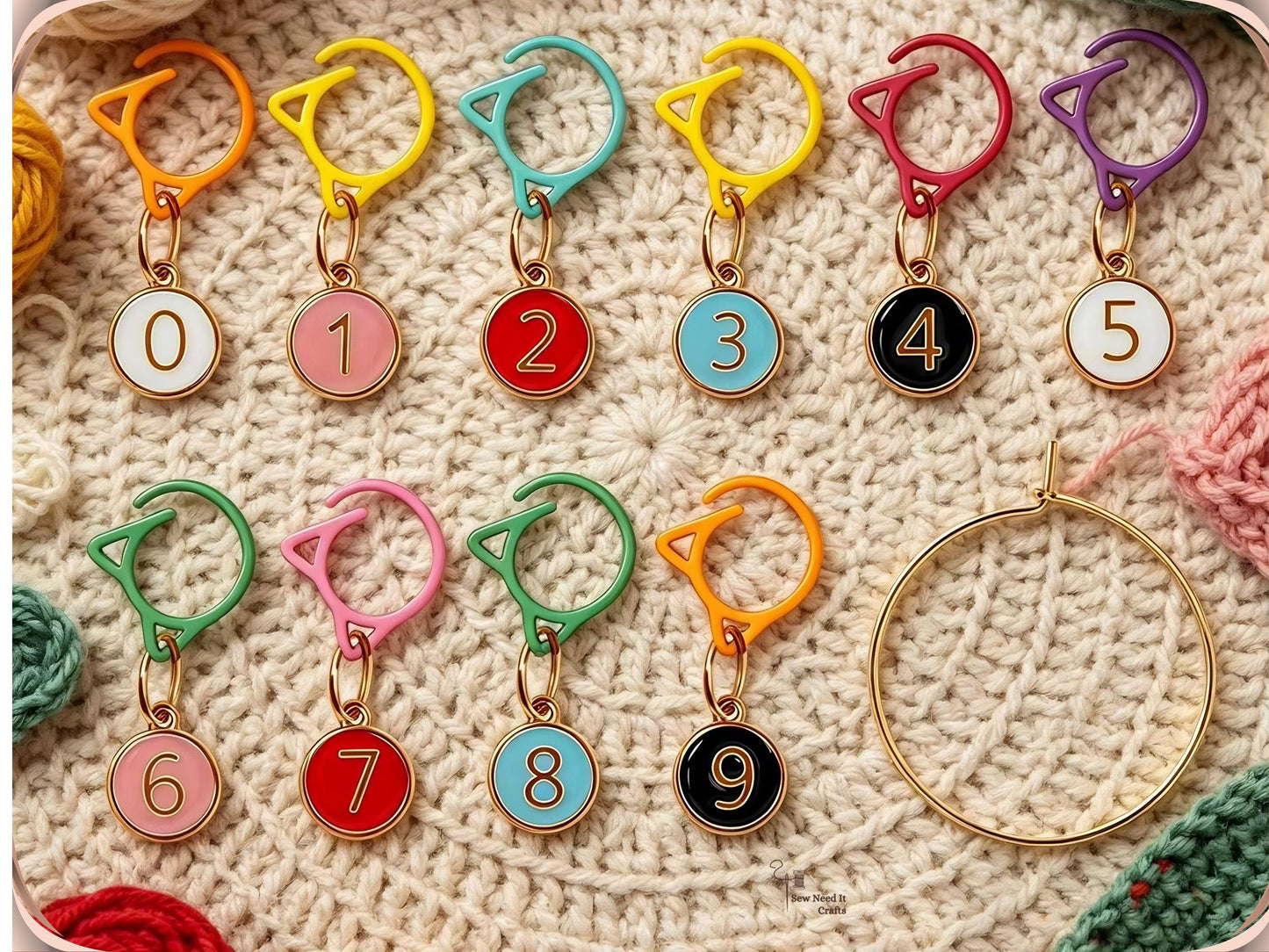 Mixed-colour numbered stitch markers 0 to 9 arranged on a cream crochet blanket with the gold-tone storage ring alongside