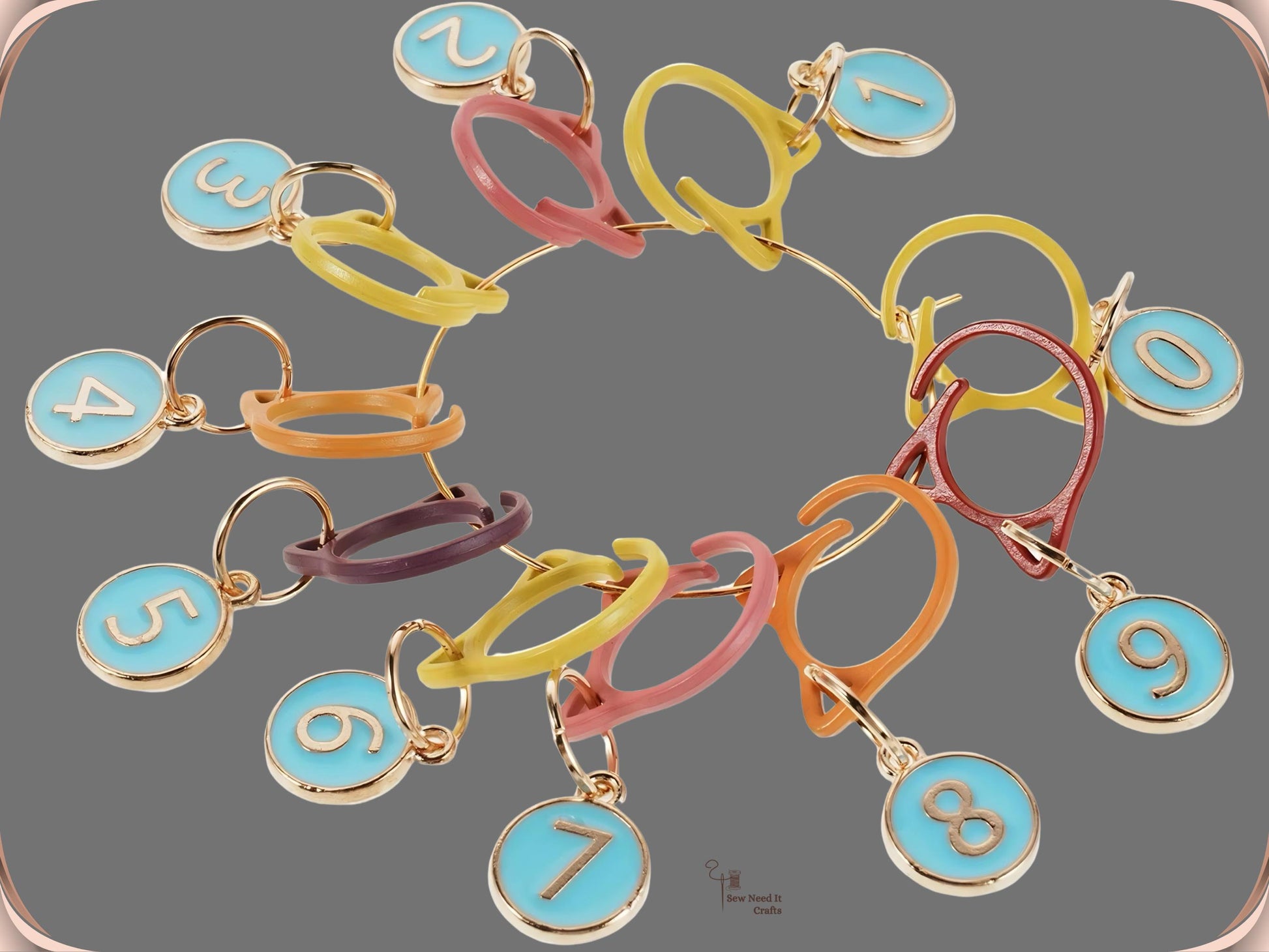 The Blue numbered stitch marker set arranged in a circle on a grey background, showing ten blue enamel charms numbered 0 to 9 on assorted-colour cat-ear clips