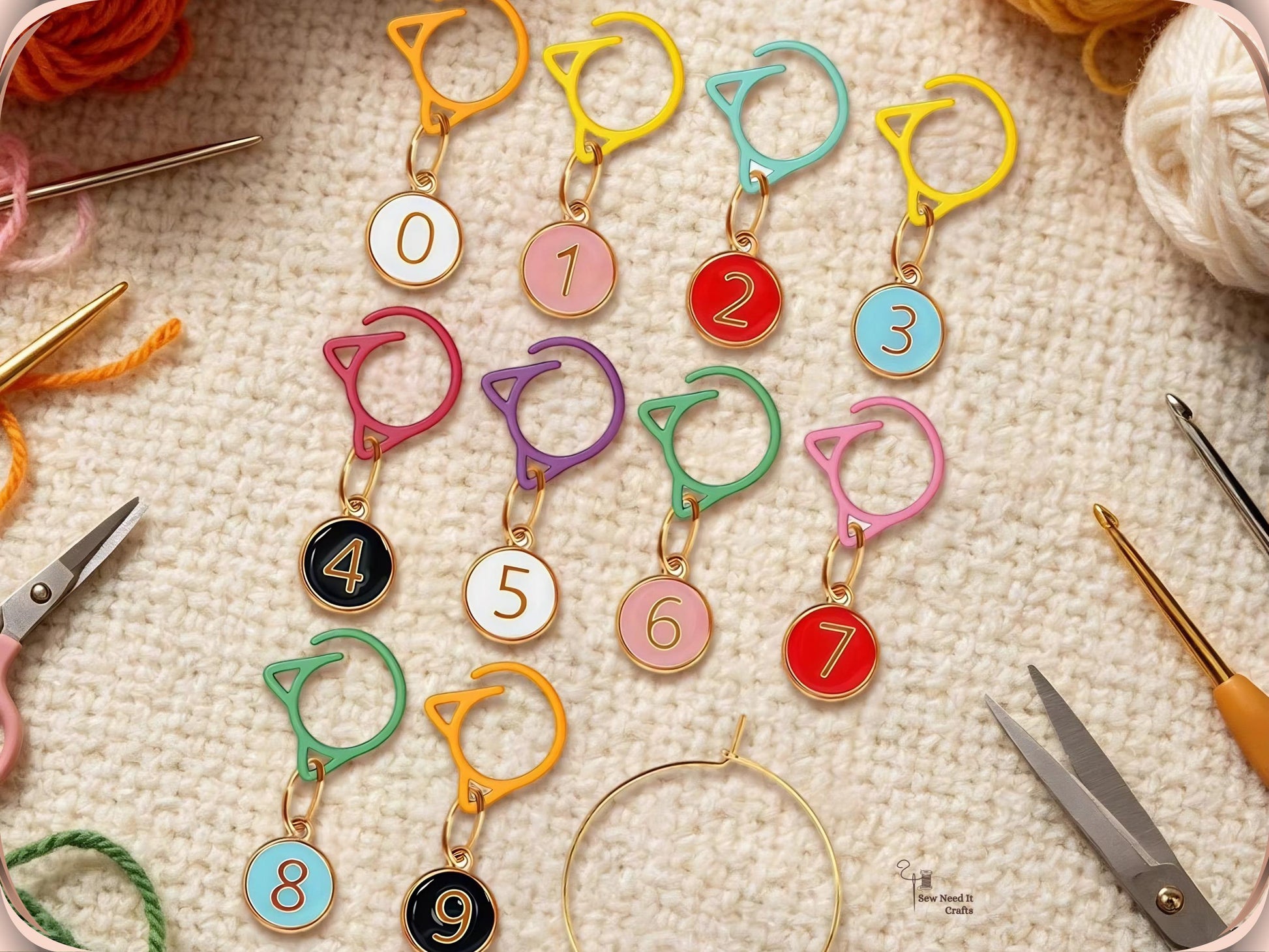 The mixed-colour numbered stitch marker set arranged on cream fabric with embroidery scissors, a crochet hook and balls of yarn