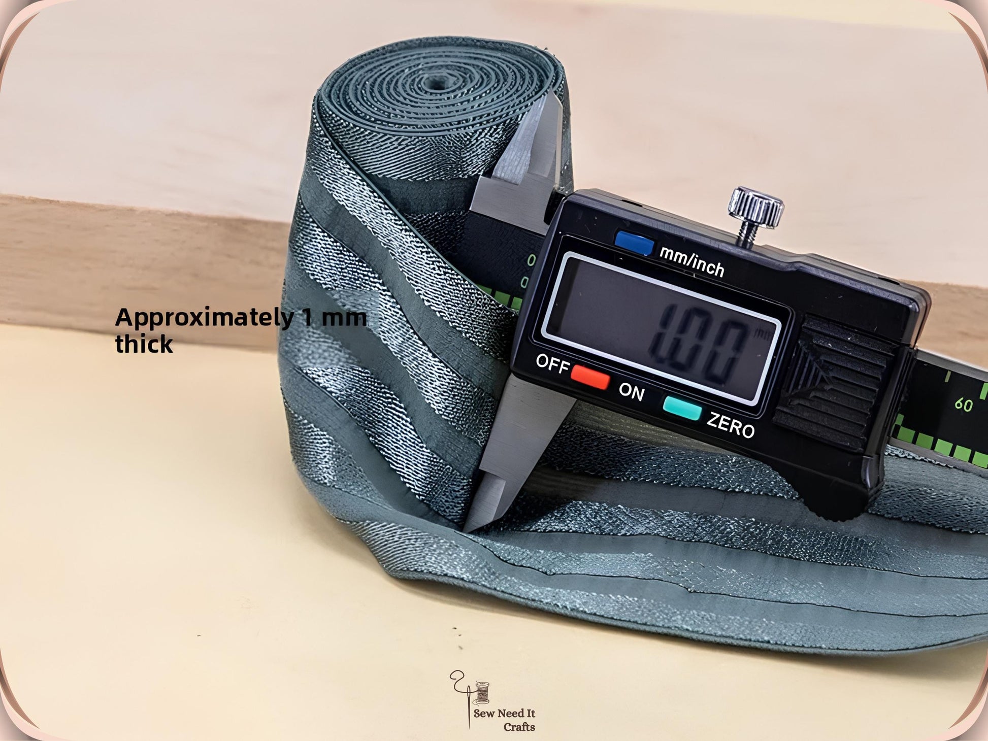 Digital caliper measuring a sage green striped elastic band at approximately 1 mm thick