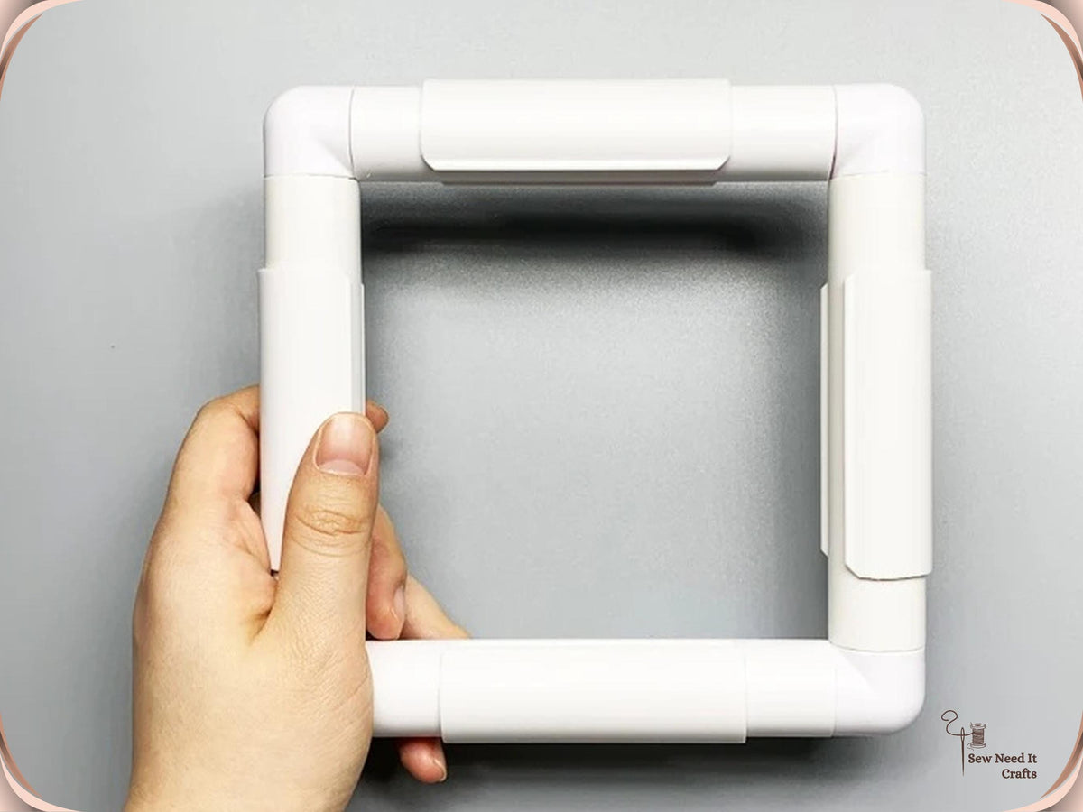 Hand holding an empty white square snap frame showing the rails, corner elbows and clamps