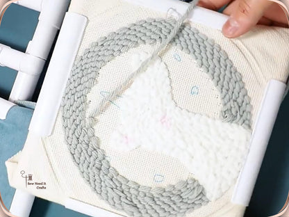 Grey and white punch needle design in progress on cream cloth clamped in a square snap frame