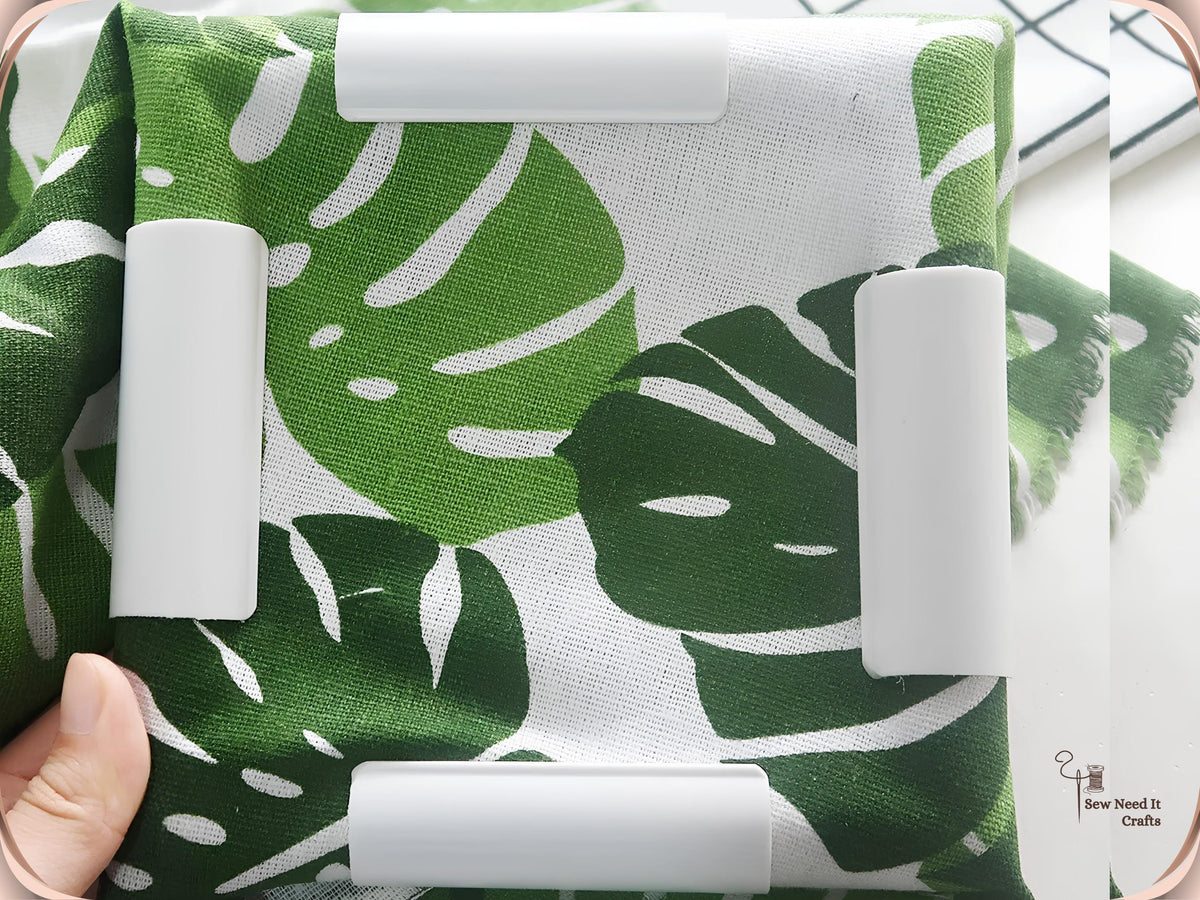 Green and white leaf-print fabric held flat in a square snap frame by four white clamps