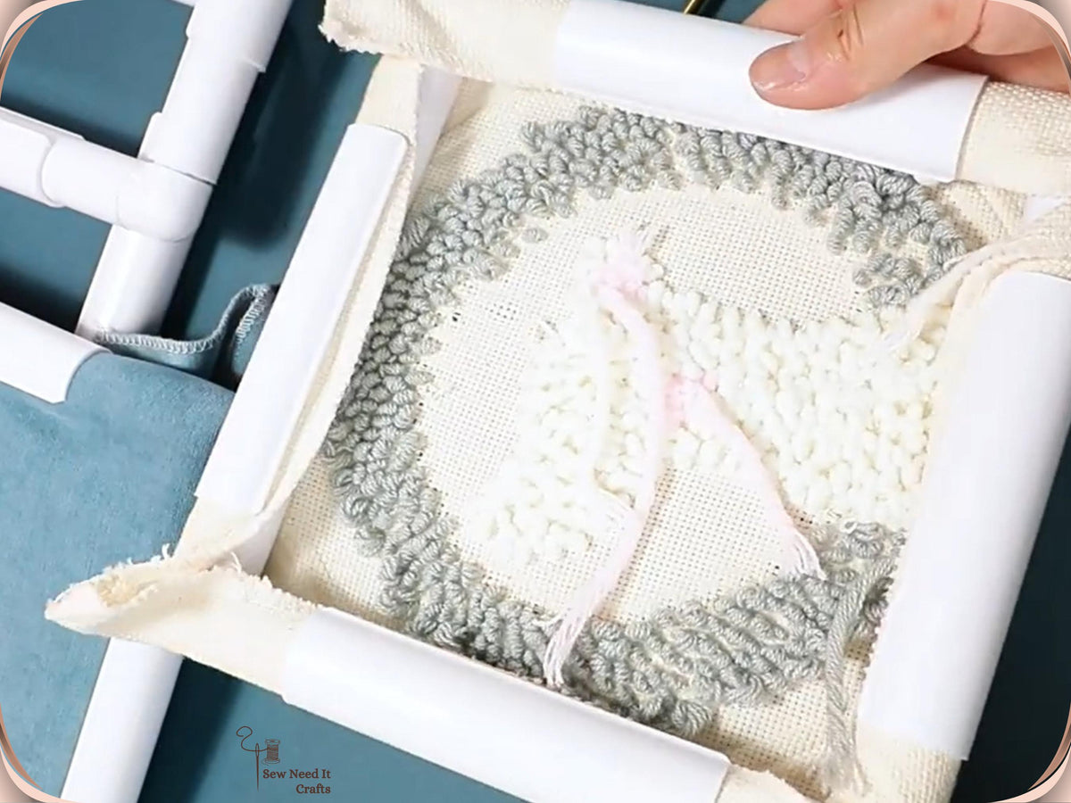 Close-up of looped grey and white punch needle work held tight in a white snap frame