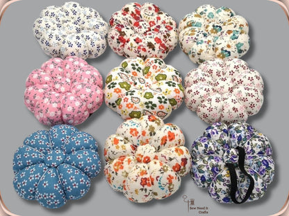Nine fabric pumpkin wrist pin cushions in assorted floral prints with black elastic bands