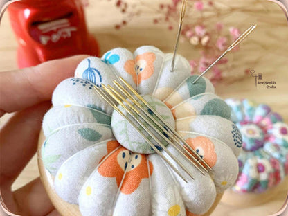 Hand holding a white floral wooden-base pin cushion with several sewing needles held flat on the magnetic center button