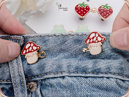 Hand fitting red mushroom waist pins to a jeans waistband, with strawberry and frog pairs behind