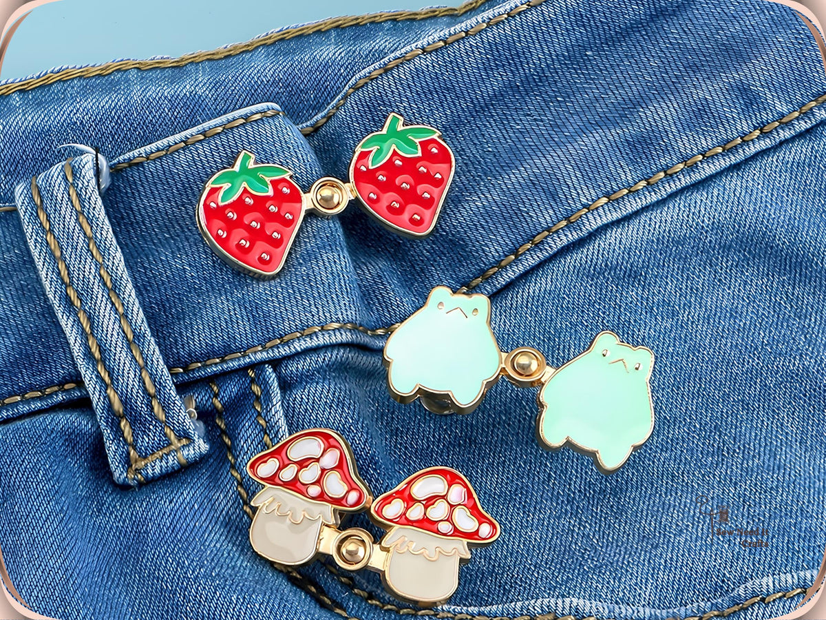 Strawberry, frog and mushroom waist tightener pins each snapped together on a denim waistband