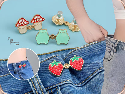 Strawberry, mushroom and frog waist tightener pins with silver back caps, and a strawberry pair snapped onto a jeans waistband