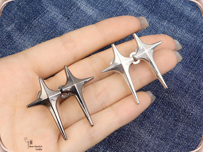 Hand holding gunmetal and silver sparkle star jean pins, each pair hooked together