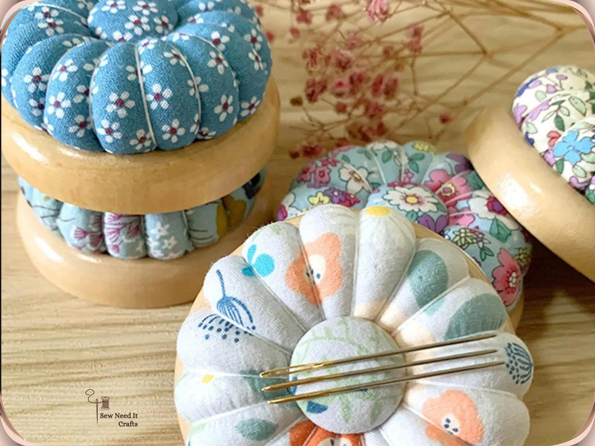 Stacked wooden-base pumpkin pin cushions, with sewing needles held on the magnetic center of a white floral one