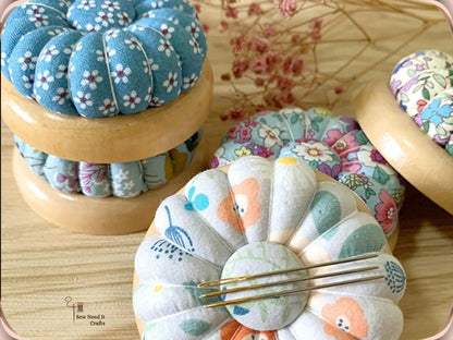Stacked wooden-base pumpkin pin cushions, with sewing needles held on the magnetic center of a white floral one