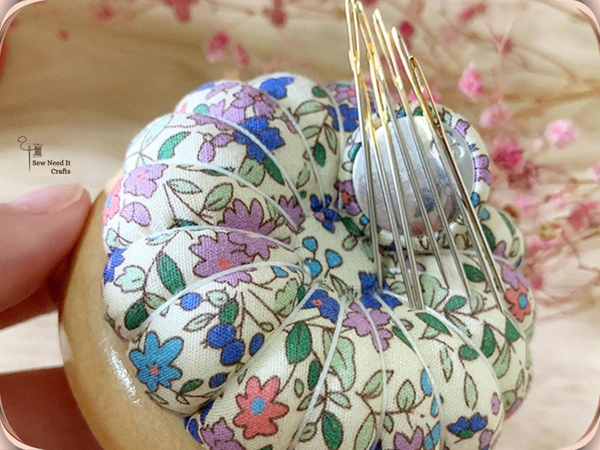 Close-up of a multicolor floral pin cushion on a wooden base with a bundle of needles held upright by the magnetic center