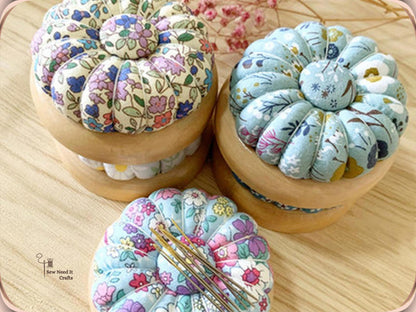 Three floral pumpkin pin cushions on wooden bases, one with needles on its center button