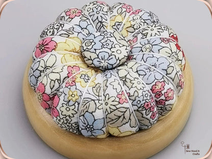 Pumpkin pin cushion in a gray and pastel line-drawn floral print on a natural wooden base