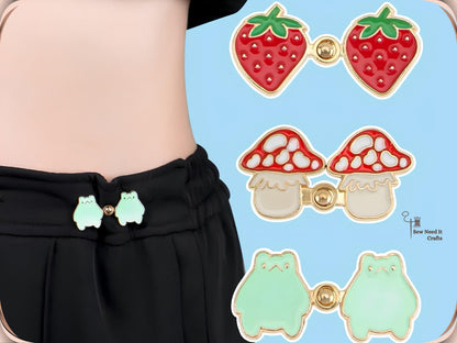 Frog waist tightener pins on black pants beside strawberry, mushroom and frog pairs snapped together