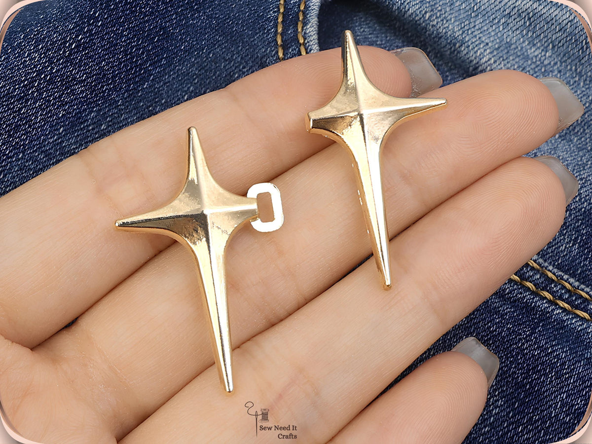 Hand holding a golden sparkle star pin with its hinged loop open beside a second golden star