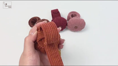 Hands demonstrating the pumpkin wrist pin cushion: the corduroy band is shown lying flat, then wrapped and snapped closed around a wrist, and finally holding several button-head sewing pins while worn