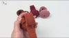 Hands demonstrating the pumpkin wrist pin cushion: the corduroy band is shown lying flat, then wrapped and snapped closed around a wrist, and finally holding several button-head sewing pins while worn