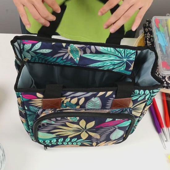 Video of the crochet and knitting project bag: yarn threaded out through one of the four holes in the top panel, several balls loaded inside, the top zipped shut, the front flap dropped to show a row of crochet hooks under an elastic band, and straight knitting needles standing in the outside side pockets