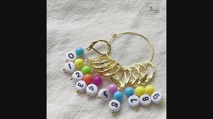 Video showing the gold set of numbered stitch markers on its storage hoop, a leverback marker opened and snapped shut by hand, and a marker clipped onto a bamboo knitting needle mid-project