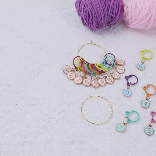 Video demonstration of the numbered cat-ear stitch markers: the full set shown on its gold-tone storage ring, then markers clipped onto a cream knitted swatch on the needles, and finally clipped into crochet worked with a hook